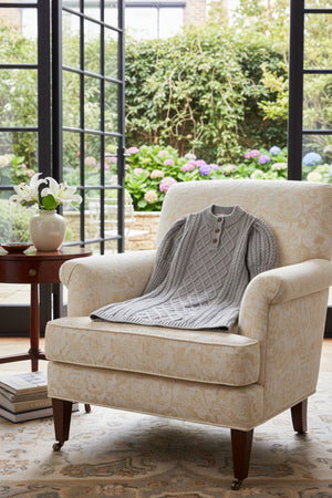 A cozy grey organic cotton sweater dress is displayed on a cream-colored armchair, with a garden view in the background.