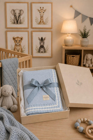 A pale blue organic cotton cable knit baby blanket is elegantly presented in a gift box, surrounded by soft toys and framed animal illustrations in a cozy nursery setting.
