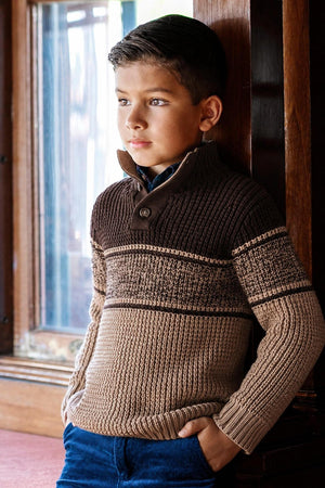 A boy stands by a window, wearing a stylish mock neck sweater featuring a textured waffle knit in camel and chocolate colors. The sweater is made from soft organic cotton.