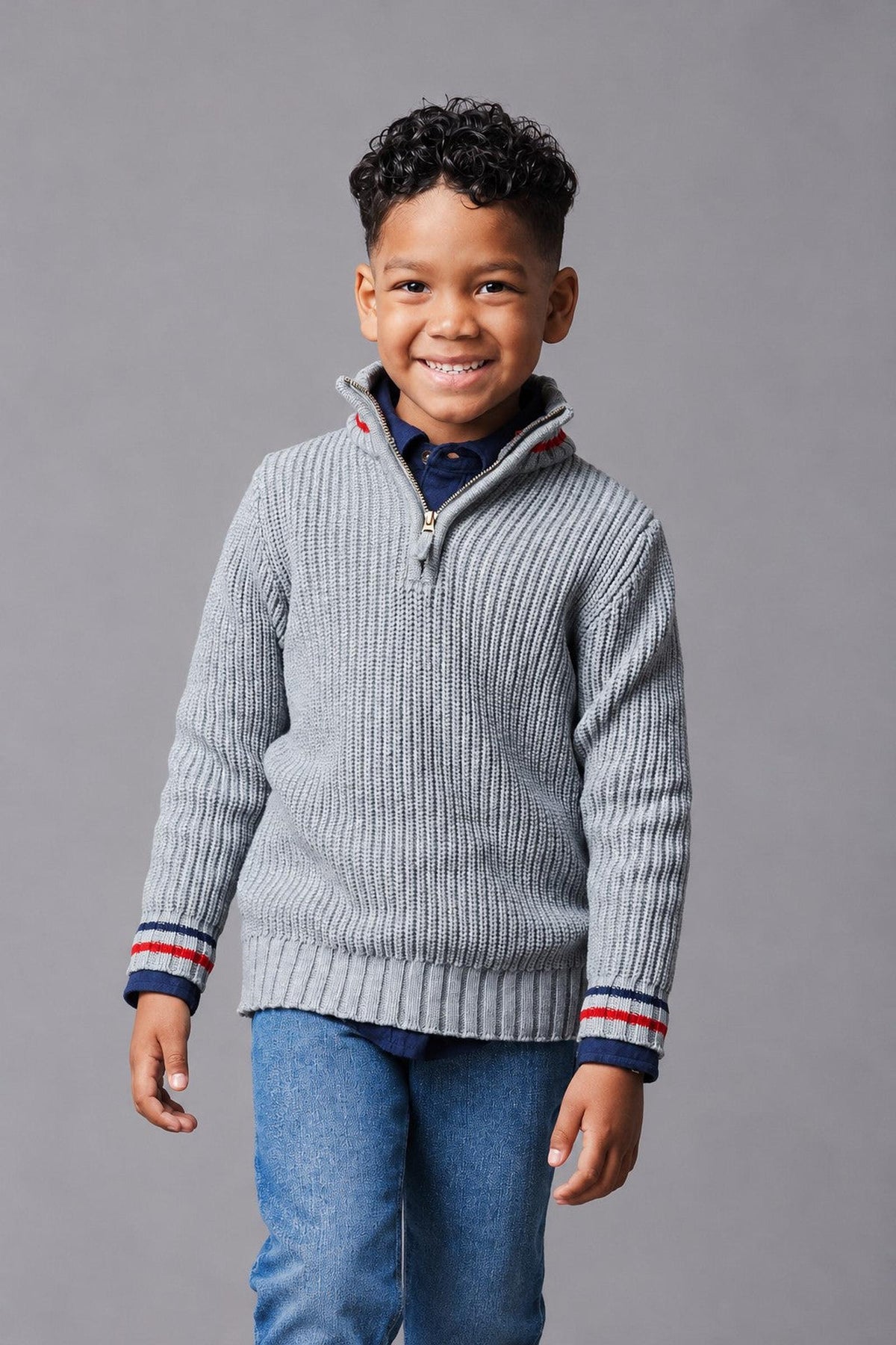 A young boy smiles while wearing a dark gray organic cotton half-zip sweater with ribbed texture and striped details.