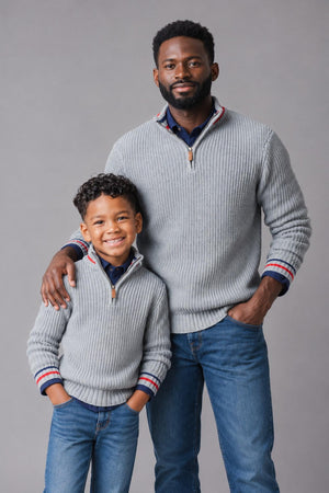 A man and a boy wear matching light gray ribbed half-zip pullovers with colorful striped accents. Both are smiling and standing against a neutral gray backdrop, showcasing a cozy, family-friendly.