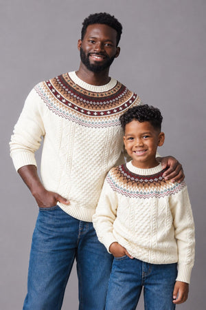A man and boy wear matching ivory sweaters with a brown and fair isle design around the shoulders.