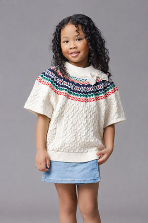A young girl with curly hair wears an ivory organic cotton mock neck sweater featuring a colorful Fair Isle pattern.