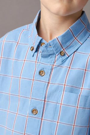 Close-up of a boy wearing a blue plaid shirt made from soft organic cotton poplin, featuring a button-down collar, chest pocket, and wooden buttons, showcasing a sustainable and classic design.