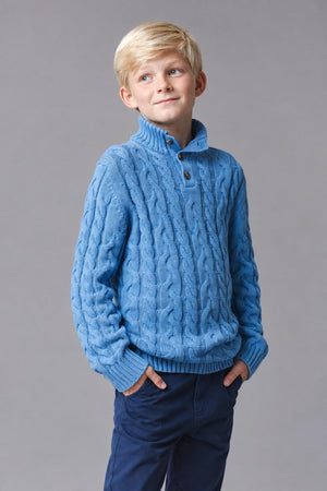 A boy models a medium blue organic cotton mock neck cable sweater with a button placket, featuring a textured knit design.