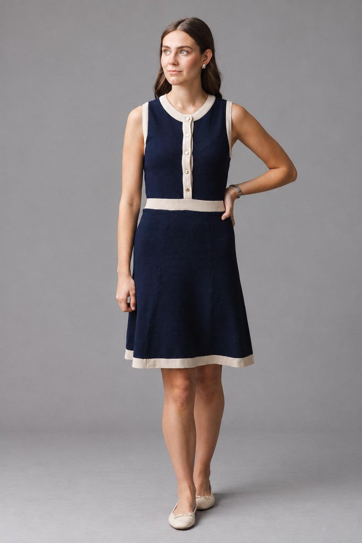A woman stands confidently in a navy organic cotton sweater dress featuring a button front, contrast rib trim, and a flared skirt. The dress is styled for a sophisticated look.