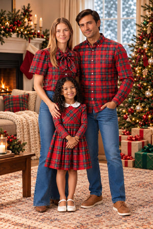 A family stands together in front of a decorated Christmas tree, wearing matching red holiday tartan outfits.
