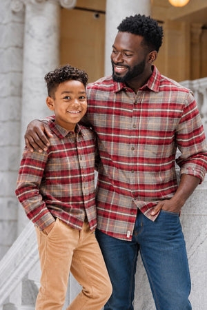 A smiling father and son wear matching organic cotton flannel shirts in rosy taupe plaid, standing together on a staircase with marble details, showcasing a cozy, family-friendly style.
