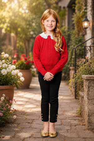 A young girl with long, wavy hair smiles while standing on a stone path surrounded by flowers.