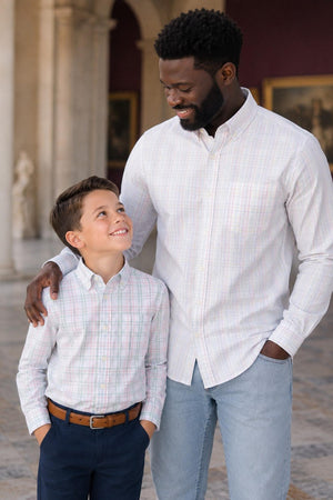 A man and a boy share a joyful moment outdoors, both wearing matching long sleeve plaid shirts.