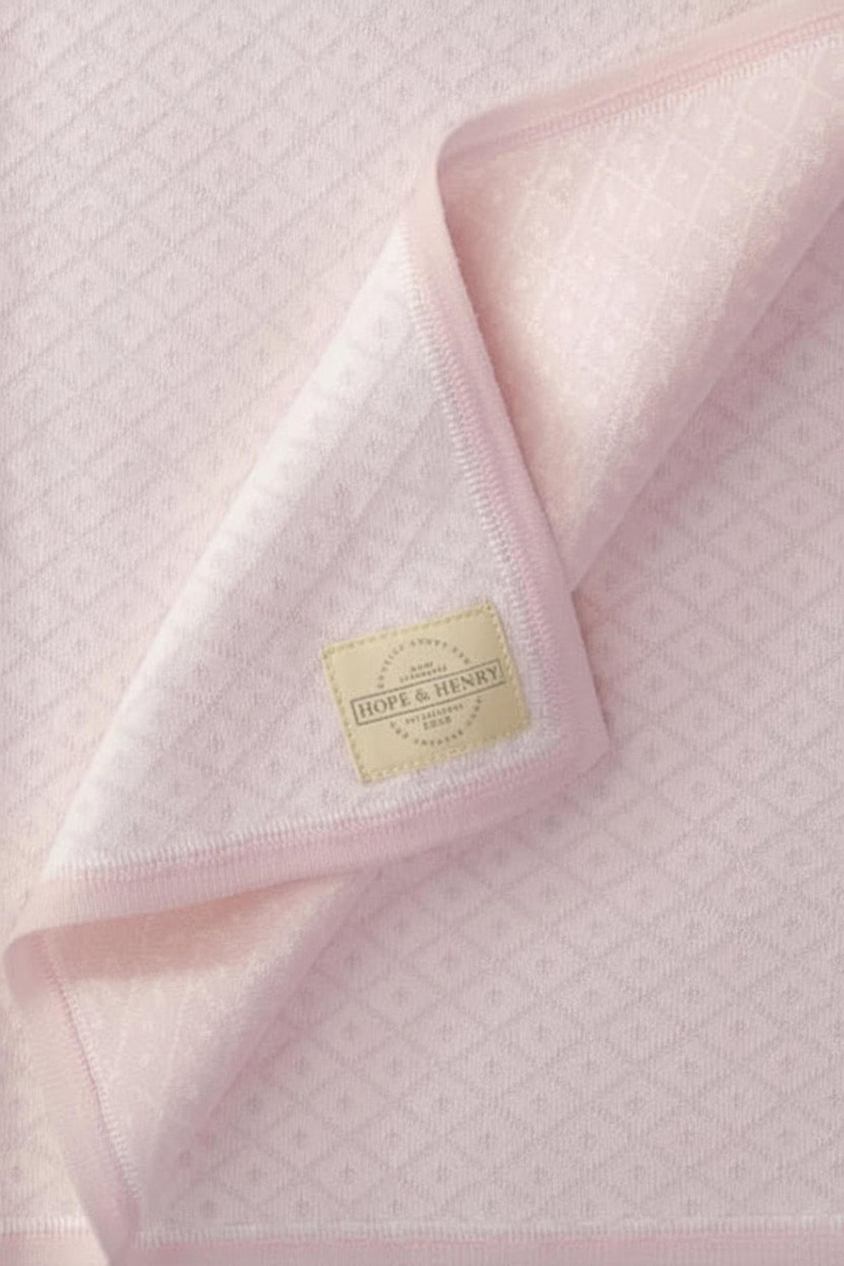 A soft pink jacquard blanket featuring a diamond pattern, with a Hope & Henry label visible on the edge.