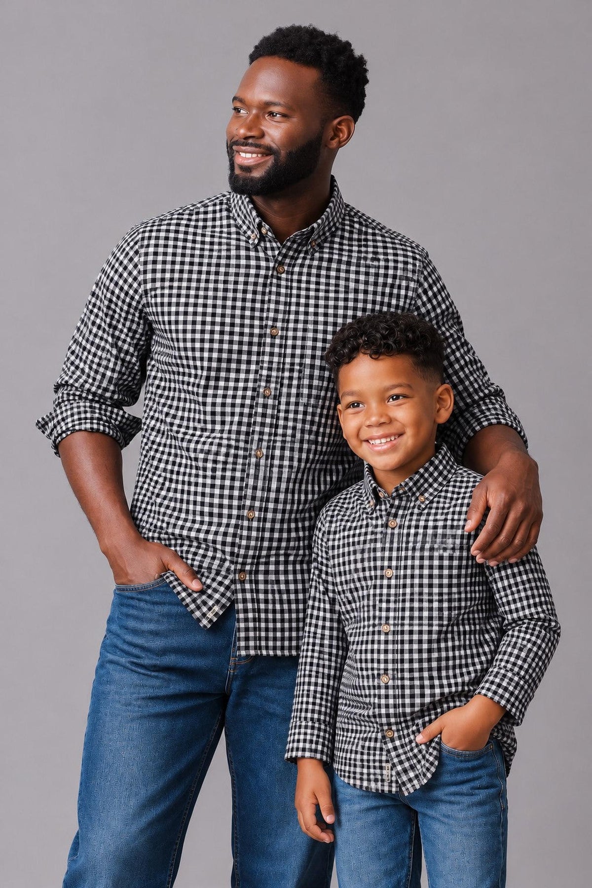 A man and a boy wear matching black gingham long-sleeve button-down shirts, showcasing a soft, organic cotton material. They stand against a neutral gray background, smiling confidently.