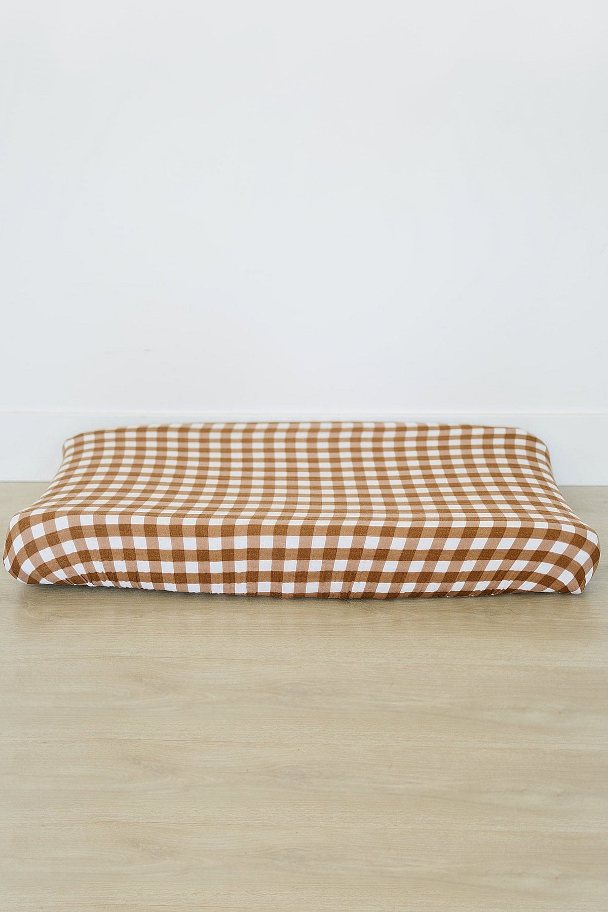 Brown and white gingham muslin changing pad cover on a wooden floor, showcasing a minimalist design.