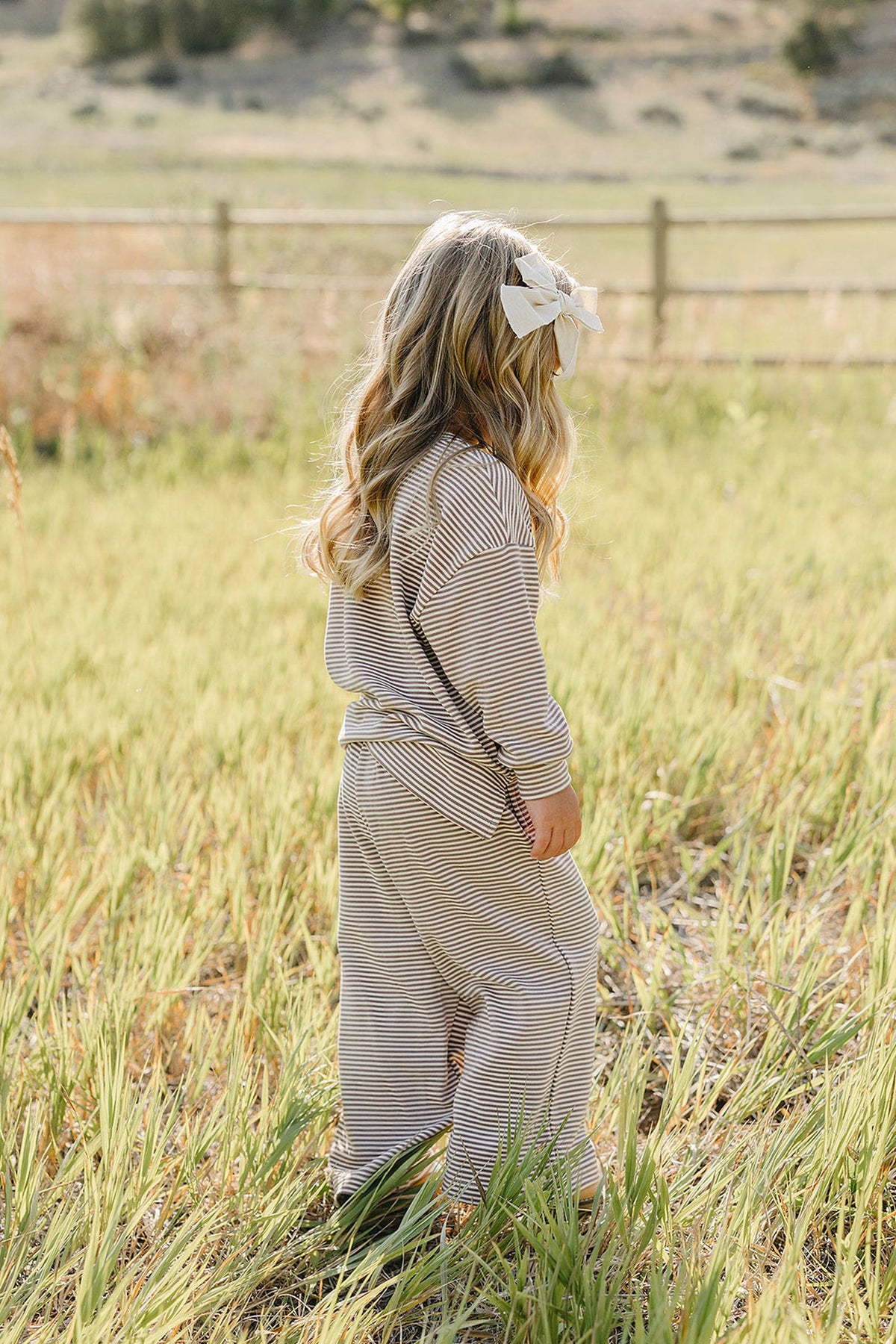 A young child wearing a soft, striped loungewear set stands in a grassy field, showcasing the comfortable outfits relaxed fit and cozy style, perfect for outdoor play.