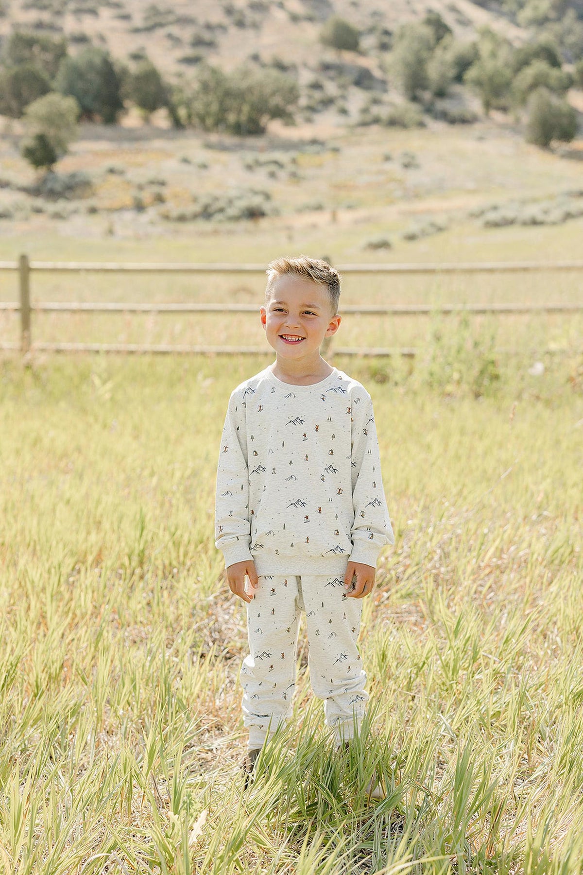 A young boy stands in a grassy field wearing a light beige French terry cotton set with playful prints. The outfit is soft, breathable, and perfect for outdoor adventures.