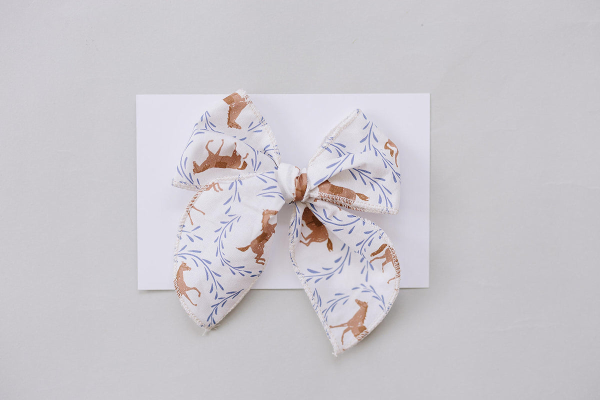 A handcrafted fabric hair bow featuring a charming pony print in earthy tones, set against a white background. Ideal for babies and kids, it combines style and comfort.