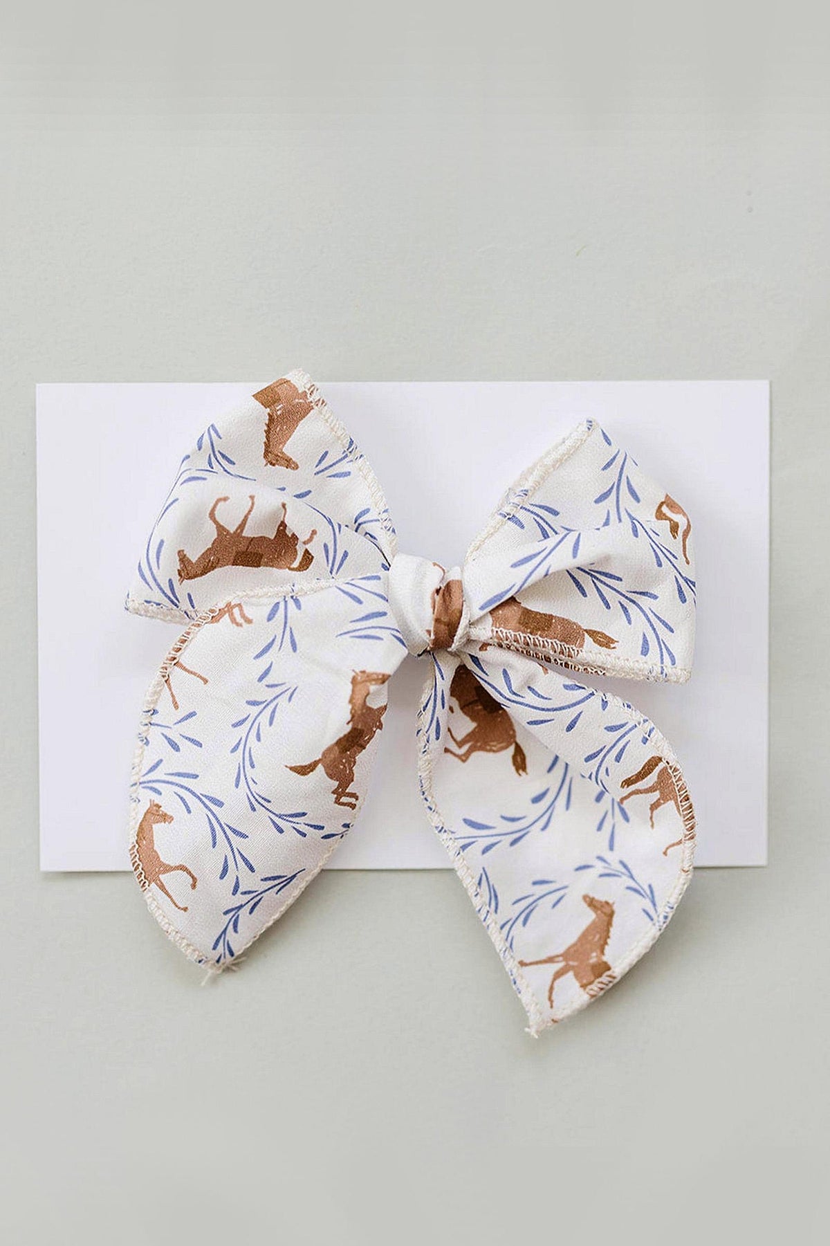 A handcrafted hair bow featuring a playful pony print in soft cotton fabric, accented with delicate blue leaves. Ideal for babies and kids, it adds charm to any outfit.