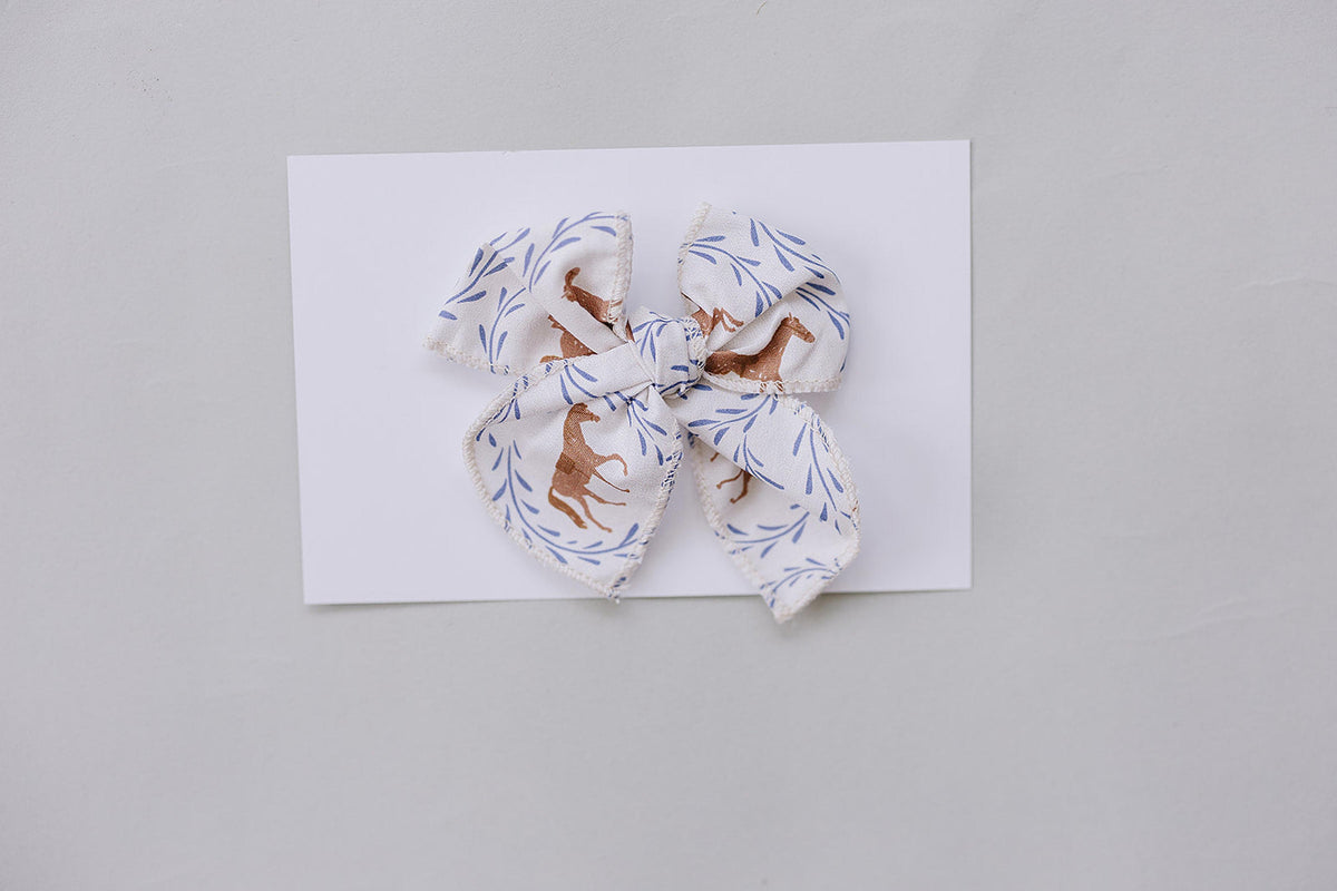 A charming Western pony print hair bow in soft cotton fabric features a light background with horse illustrations and delicate foliage.