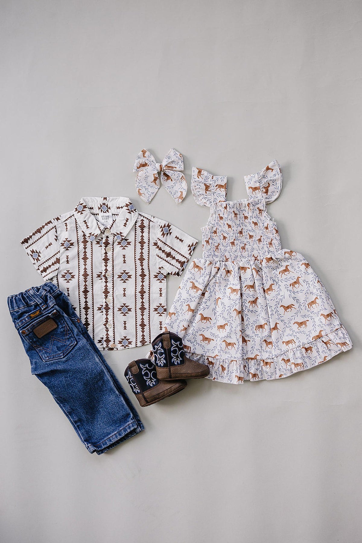 A stylish Aztec Western button-up shirt with a geometric pattern is paired with a matching dress, denim jeans, and coordinating hair accessories, showcasing a charming, coordinated outfit for kids.