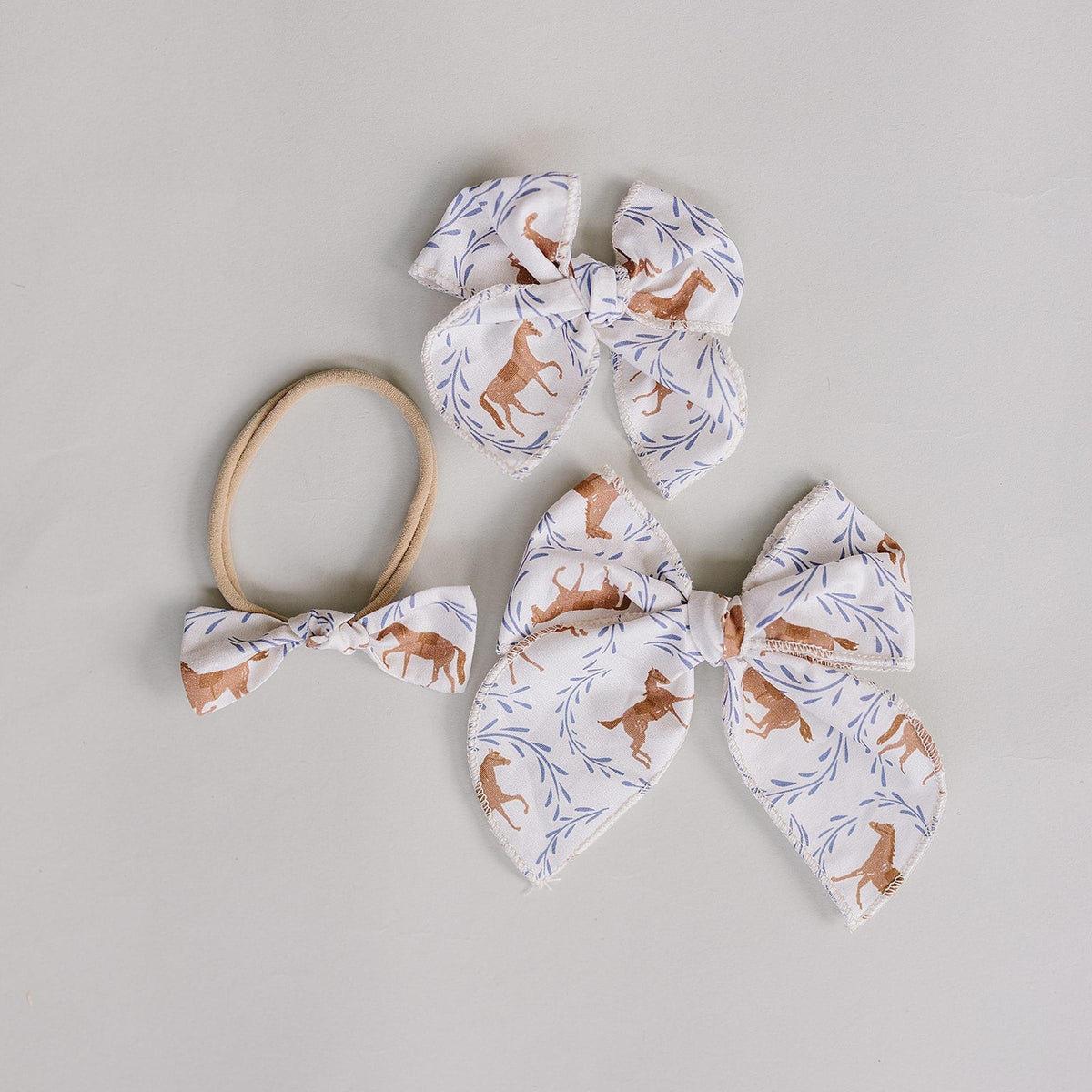 Three handcrafted hair bows featuring a whimsical pony print on white fabric, accompanied by a matching hair tie. Ideal for babies and kids, made from 95% cotton for comfort.