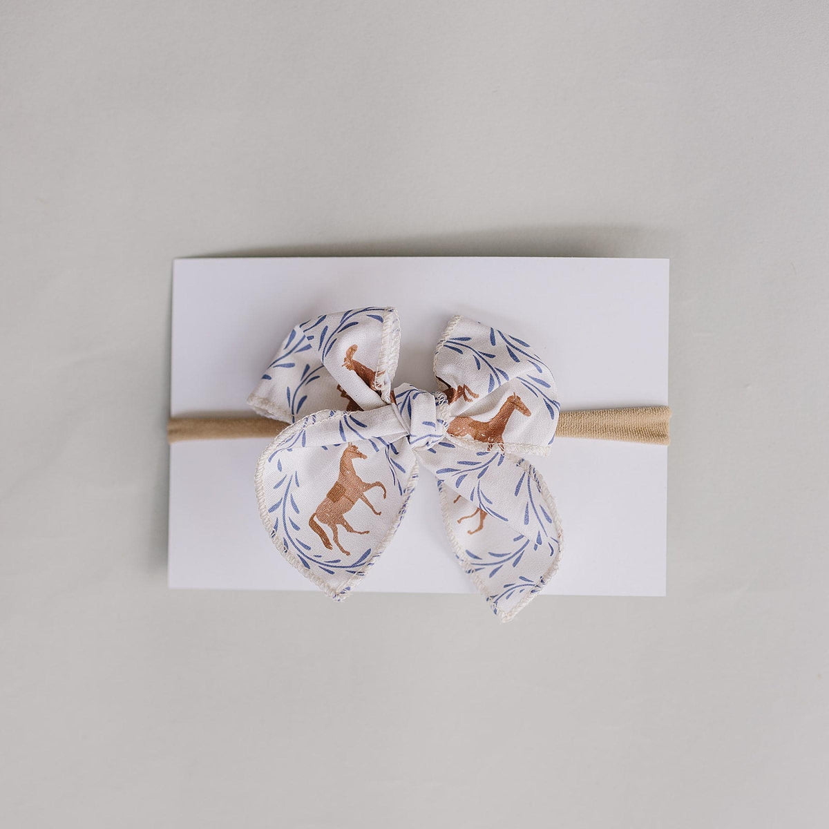 A handcrafted hair bow featuring a whimsical pony print in soft colors, elegantly tied and displayed on a white card.