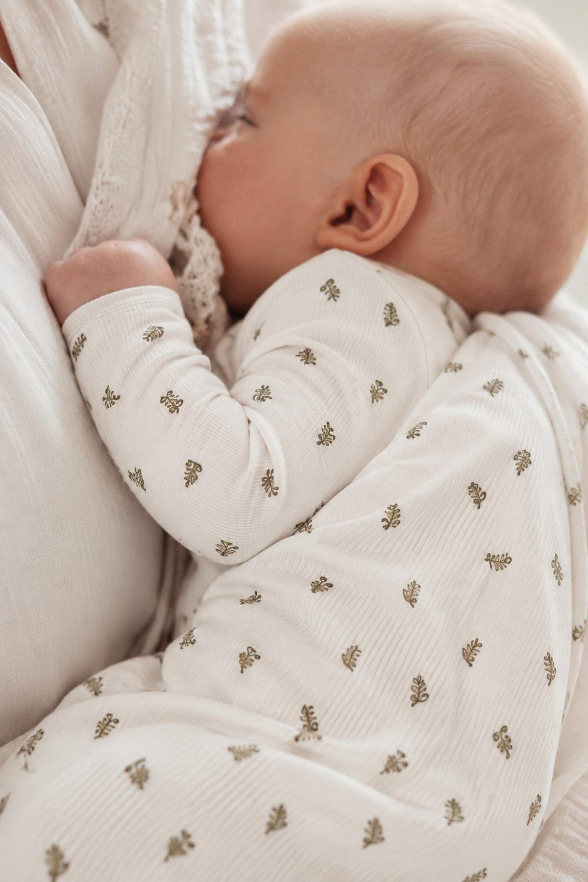 A peaceful baby sleeps against a soft, textured blanket, wearing a light-colored romper adorned with delicate leaf patterns. The fabric appears cozy, ideal for comfort and warmth.