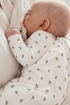 A peaceful baby sleeps against a soft, textured blanket, wearing a light-colored romper adorned with delicate leaf patterns. The fabric appears cozy, ideal for comfort and warmth.