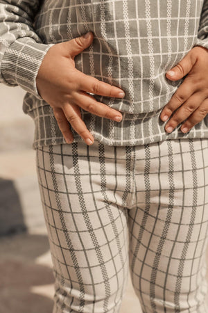 A child is wearing sage check printed cotton leggings paired with a matching top, showcasing a soft fabric blend. The outfit is cozy and perfect for everyday wear and play.