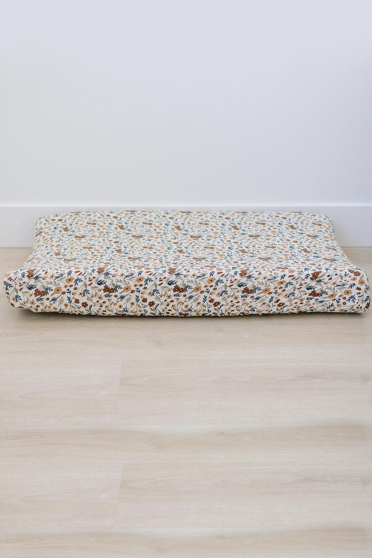Floral-patterned changing pad cover on a wooden floor, showcasing a mix of brown, blue, and white colors.