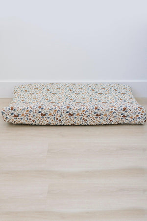 Floral-patterned changing pad cover on a wooden floor, showcasing a mix of brown, blue, and white colors.