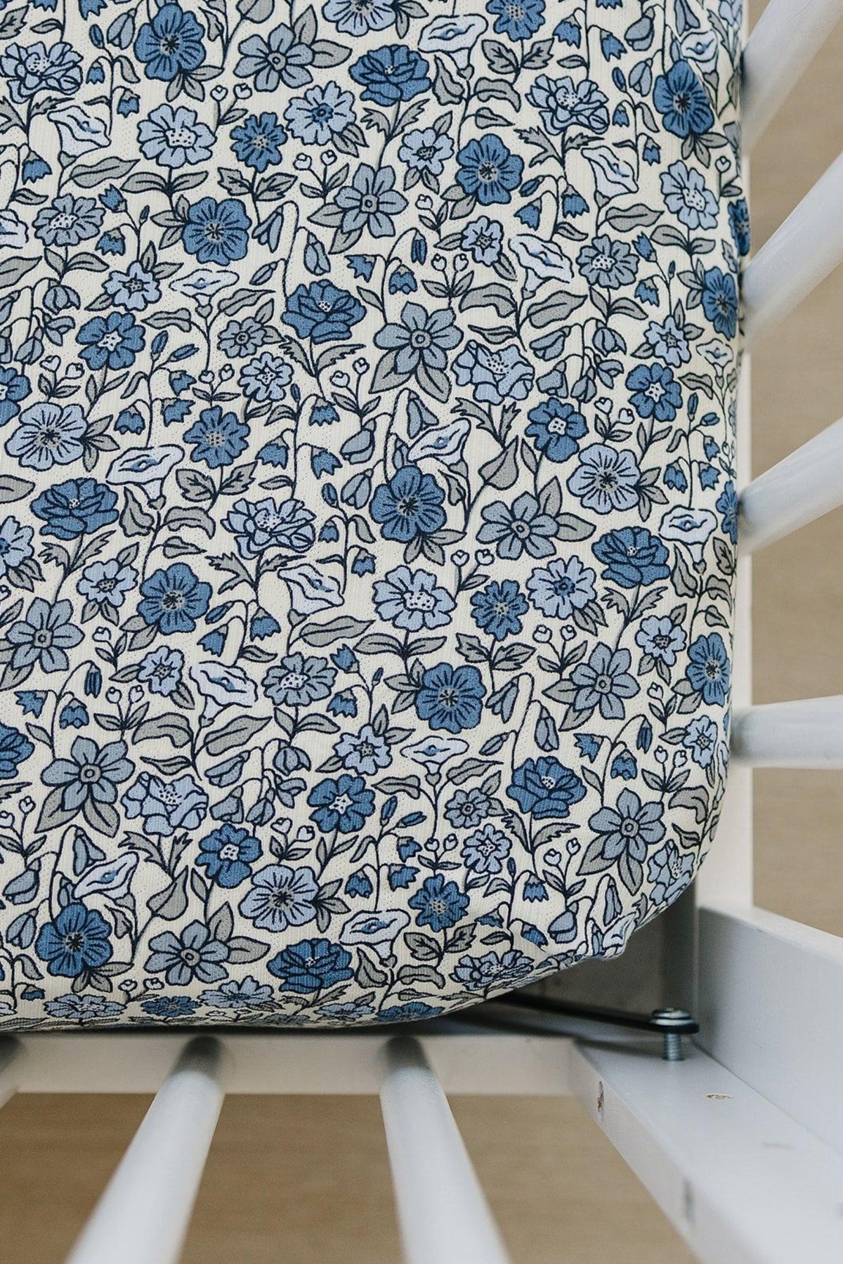 Blue and white floral crib sheet on a white crib, showcasing a detailed flower pattern and soft fabric.