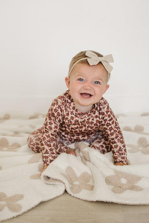 A joyful baby sits on a soft, light-colored blanket, wearing an Antique Floral Cotton Set featuring a long sleeve top with a floral pattern.
