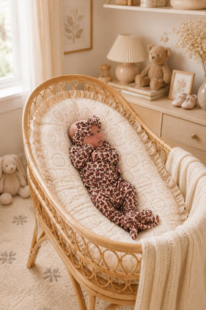 A cozy baby lies in a rattan bassinet, wearing a floral ribbed bamboo layette set. The soft, breathable fabric features deep maroon and cream patterns, perfect for everyday comfort.