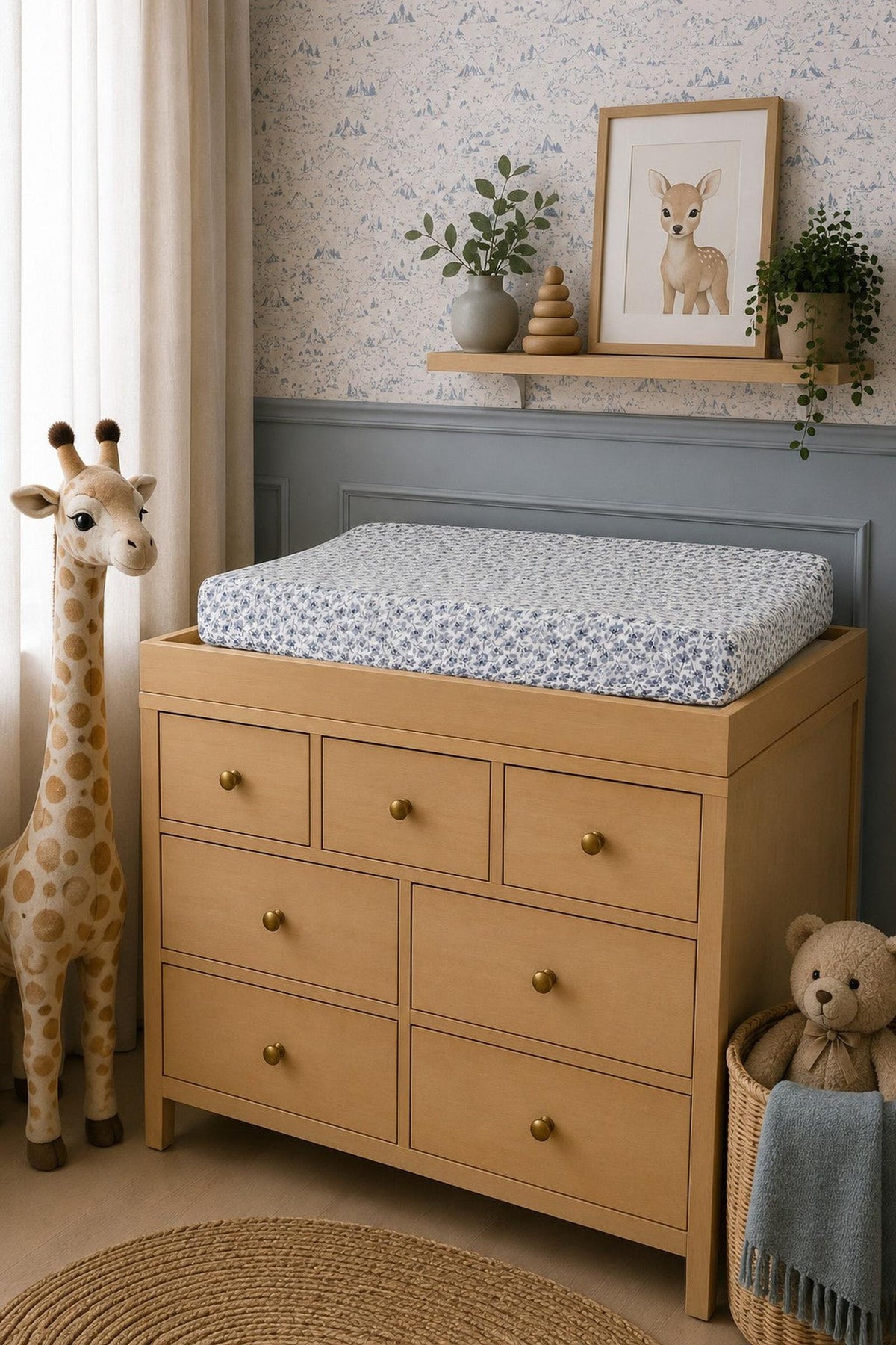 A beautifully styled nursery features a light wooden changing table with a blue floral muslin changing pad cover.