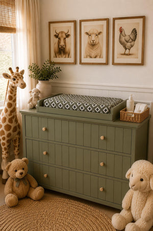 A cozy nursery features a green dresser topped with a patterned changing pad, surrounded by plush toys and framed animal art on the wall, creating a warm, inviting atmosphere.