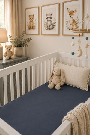 A cozy nursery features a white crib with a deep navy fitted sheet, a plush bunny toy, and decorative wall art of animals.