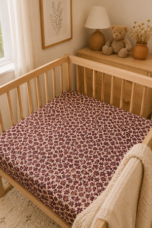 A cozy nursery setting features a wooden crib with a floral ribbed bamboo crib sheet in deep burgundy and cream tones, enhancing the soft, inviting atmosphere for peaceful baby naps.