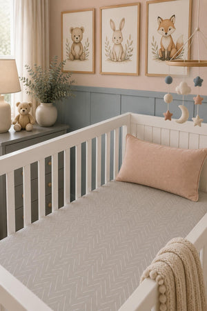 A cozy nursery features a white crib with a soft, gray herringbone-patterned muslin crib sheet. Decorative animal artwork and a mobile adorn the pastel walls, creating a serene environment.