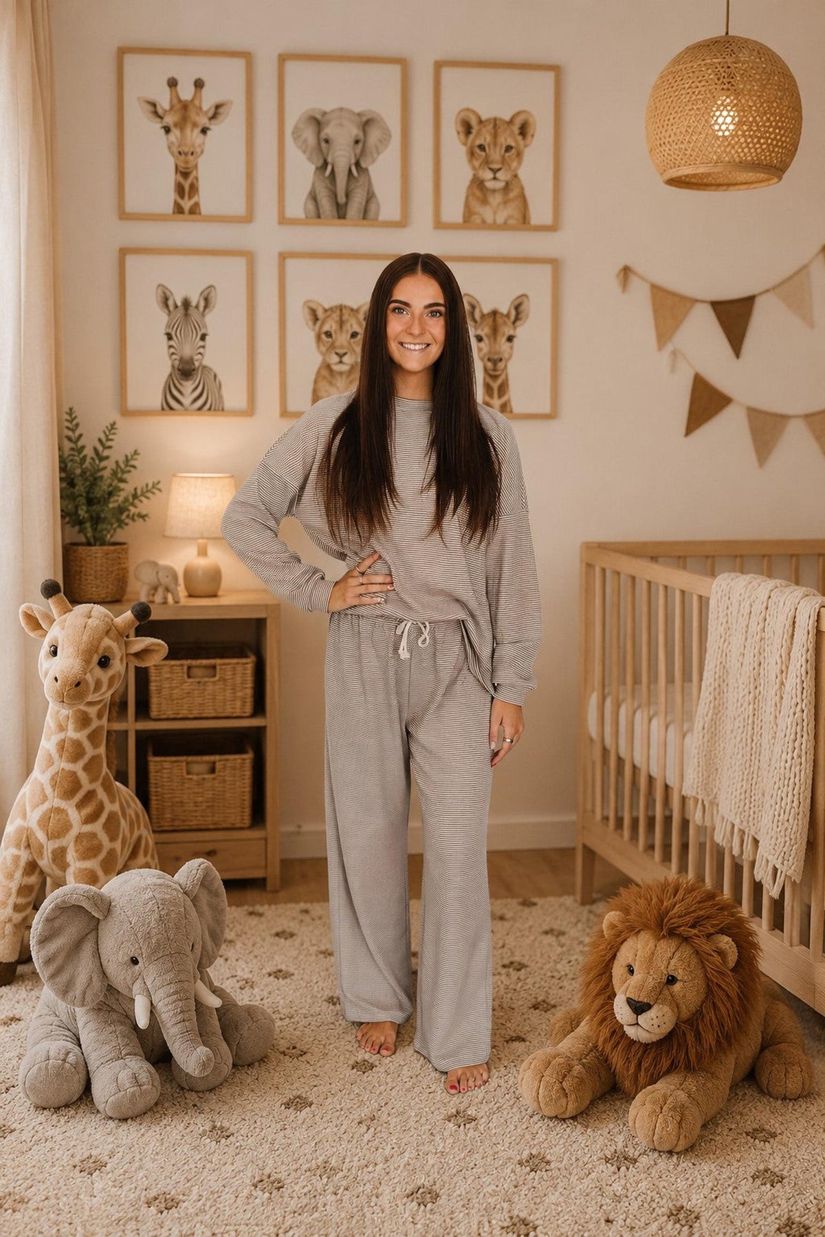 A woman stands in a cozy nursery, wearing a soft gray loungewear set made from breathable cotton. The room features animal-themed decor, a crib, and plush toy elephants and lions.