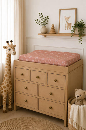 A soft, peach-colored muslin changing pad cover with a floral pattern rests on a wooden changing table.