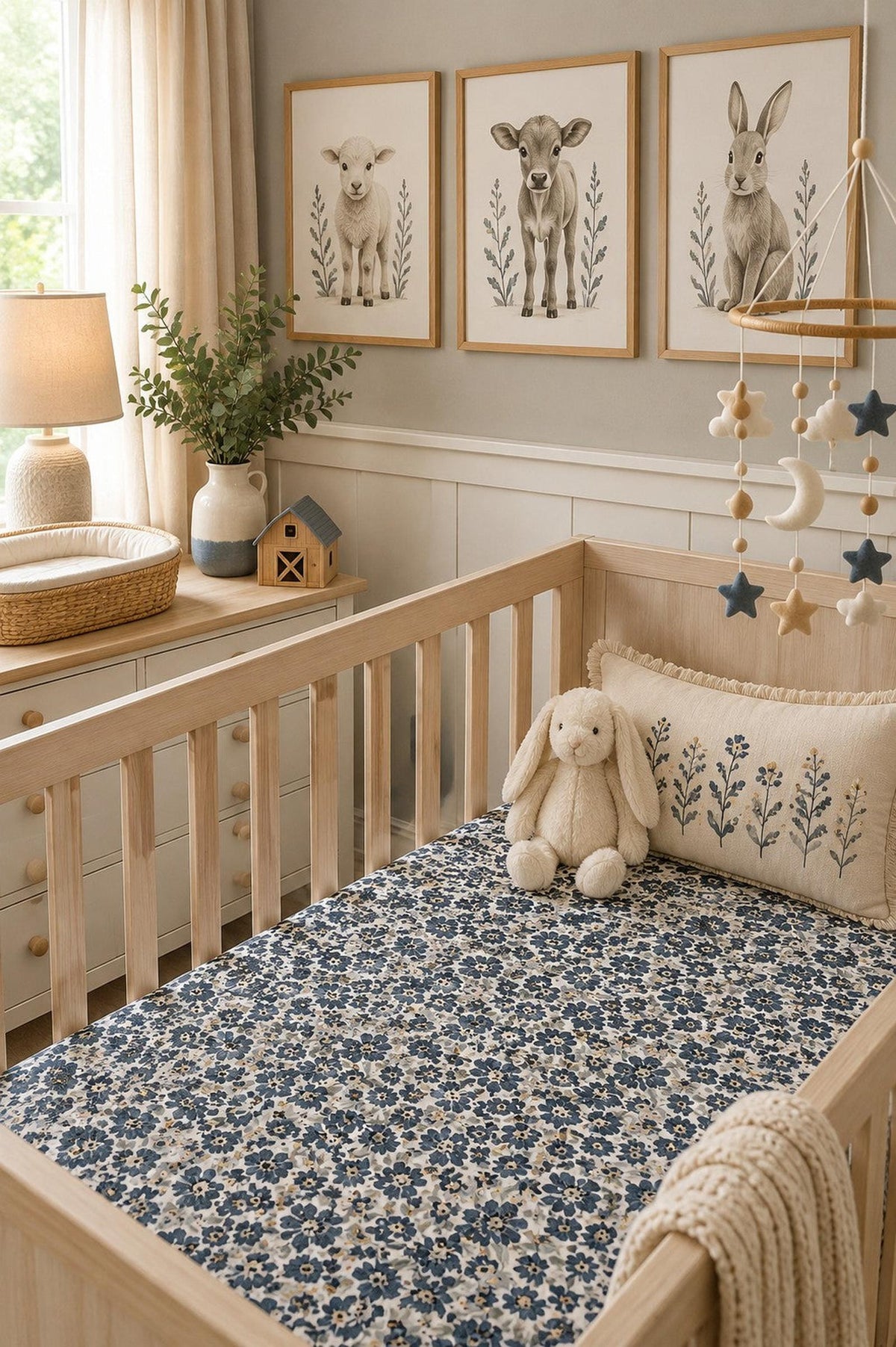 A beautifully styled nursery features a wooden crib with a Liberty Floral Muslin Crib Sheet in blue and gray, complemented by charming animal artwork and soft decorative elements.