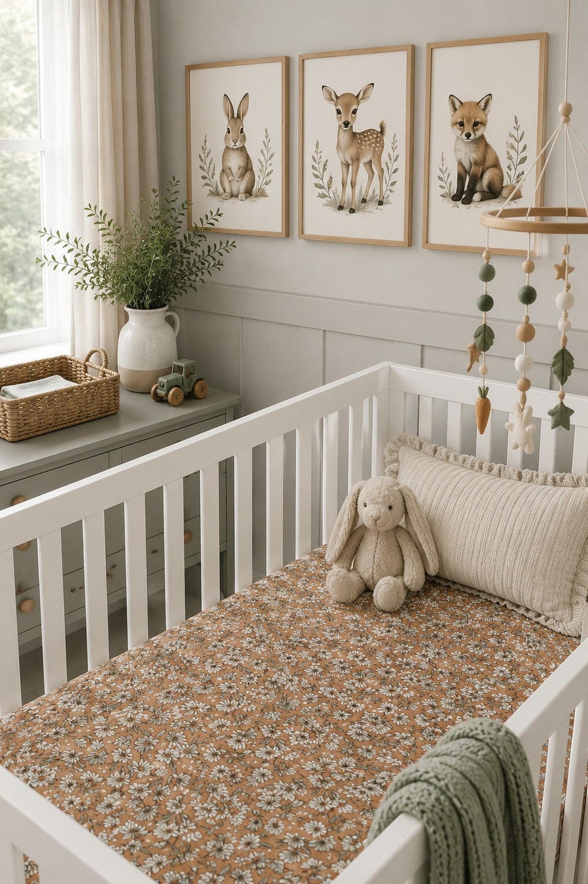 A cozy nursery features a white crib with a floral-patterned muslin crib sheet. The room is decorated with animal prints, a plush bunny, and soft green accents.