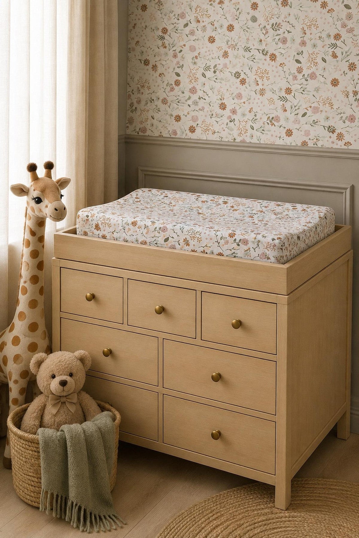 A wooden changing table with a Meadow Floral muslin changing pad cover sits against a floral wallpaper backdrop.