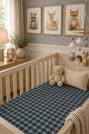A cozy nursery features a wooden crib with a navy plaid muslin crib sheet. Soft toys and decorative elements create a warm, inviting atmosphere, perfect for a babys comfort.