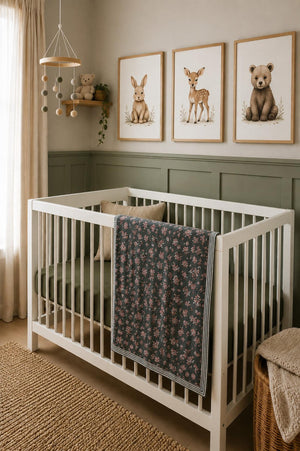 A cozy nursery featuring a white crib with a dark floral muslin quilt draped over the side, surrounded by soft green walls and charming animal artwork above.