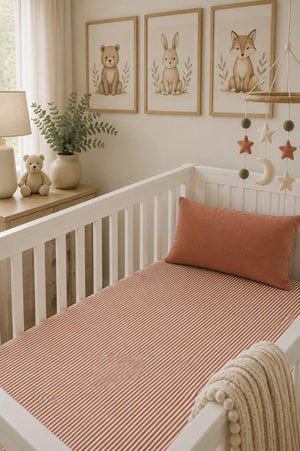 A cozy nursery featuring a white crib with a pink striped muslin crib sheet and a decorative pillow. Framed animal illustrations and a mobile enhance the warm, inviting atmosphere.