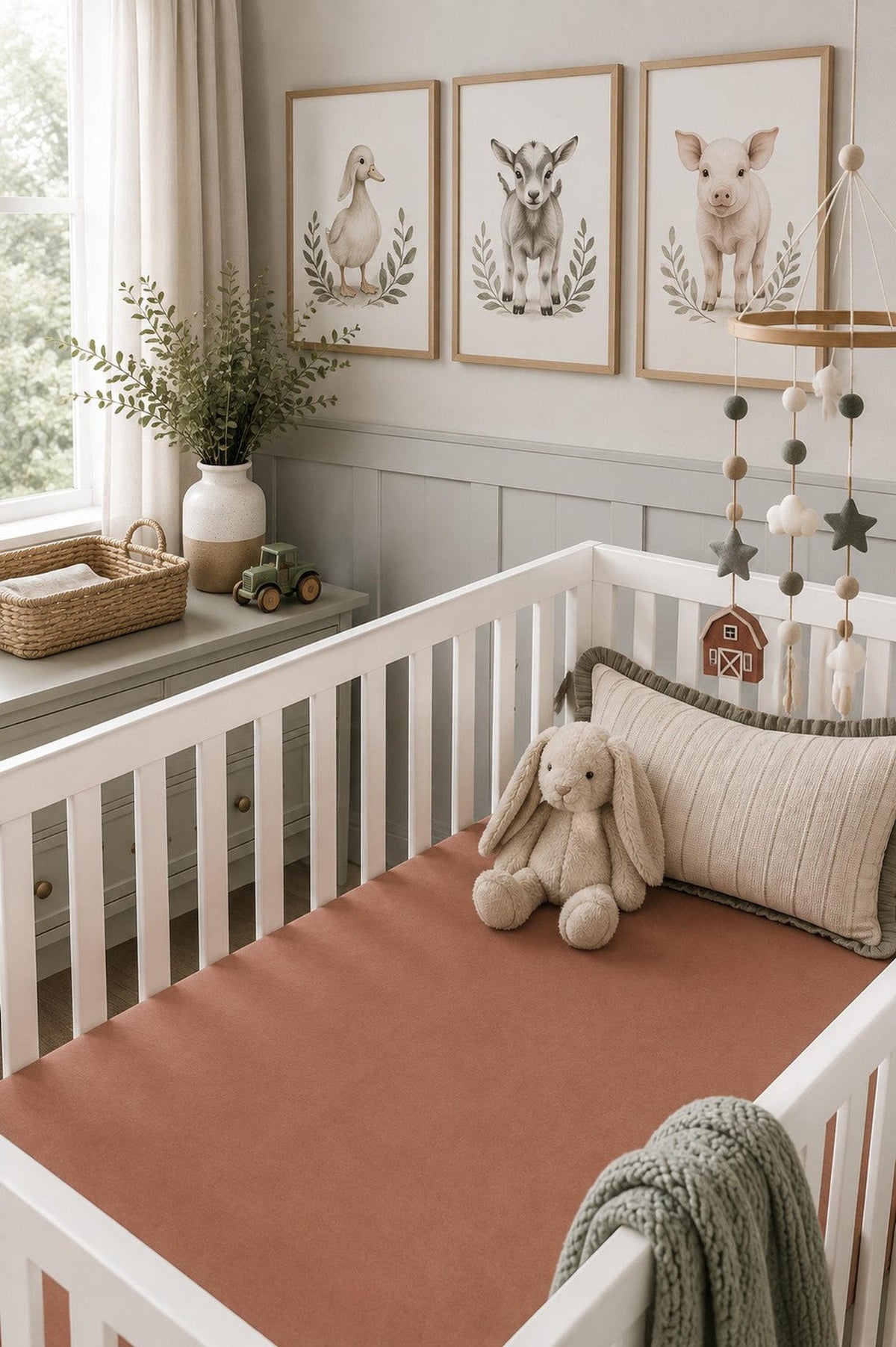A cozy nursery features a white crib with a rust-colored fitted bamboo crib sheet, a plush bunny toy, and soft decorative elements.