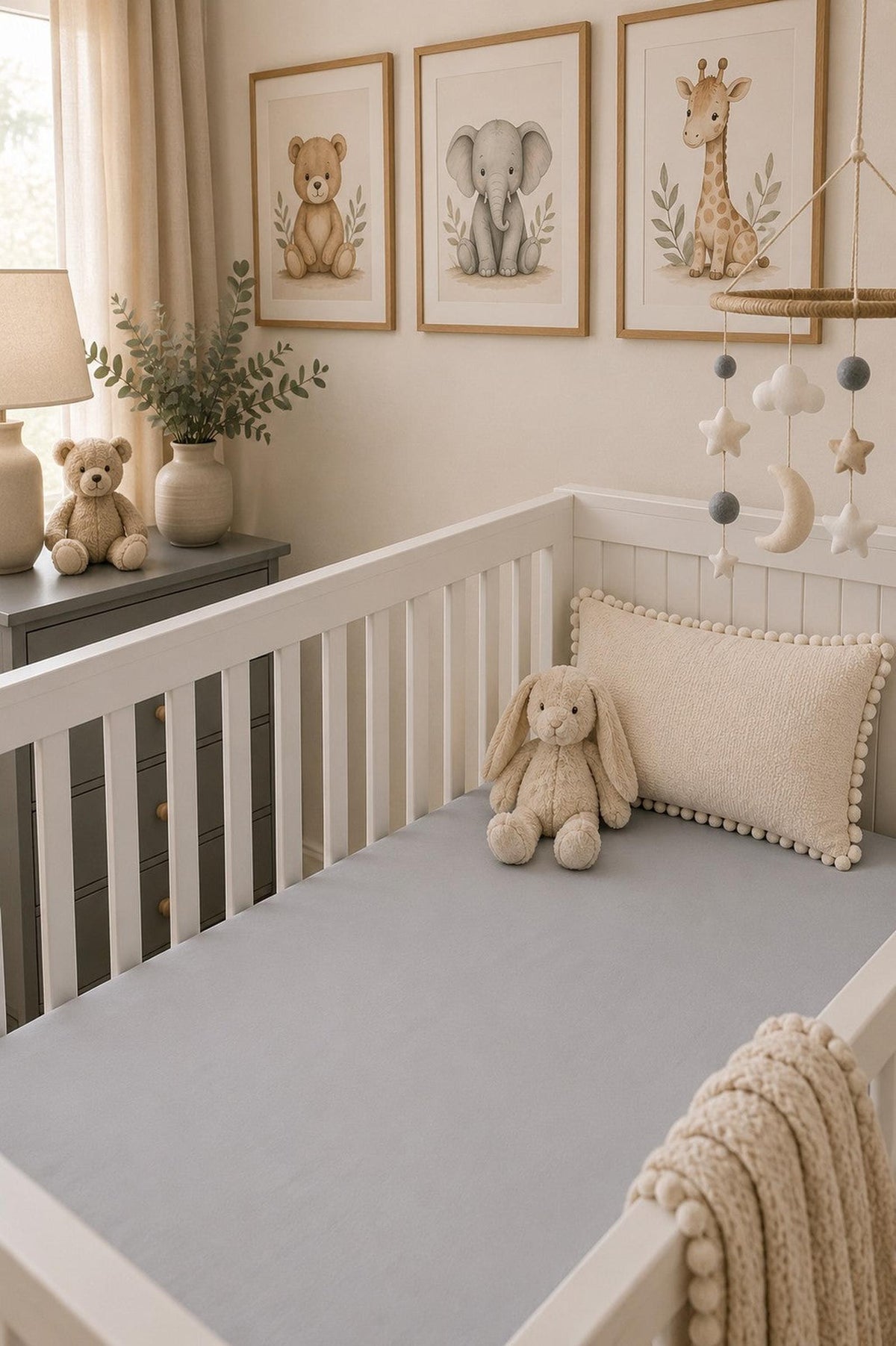 A cozy nursery features a white crib with a soft gray crib sheet, adorned with plush toys and a decorative pillow.