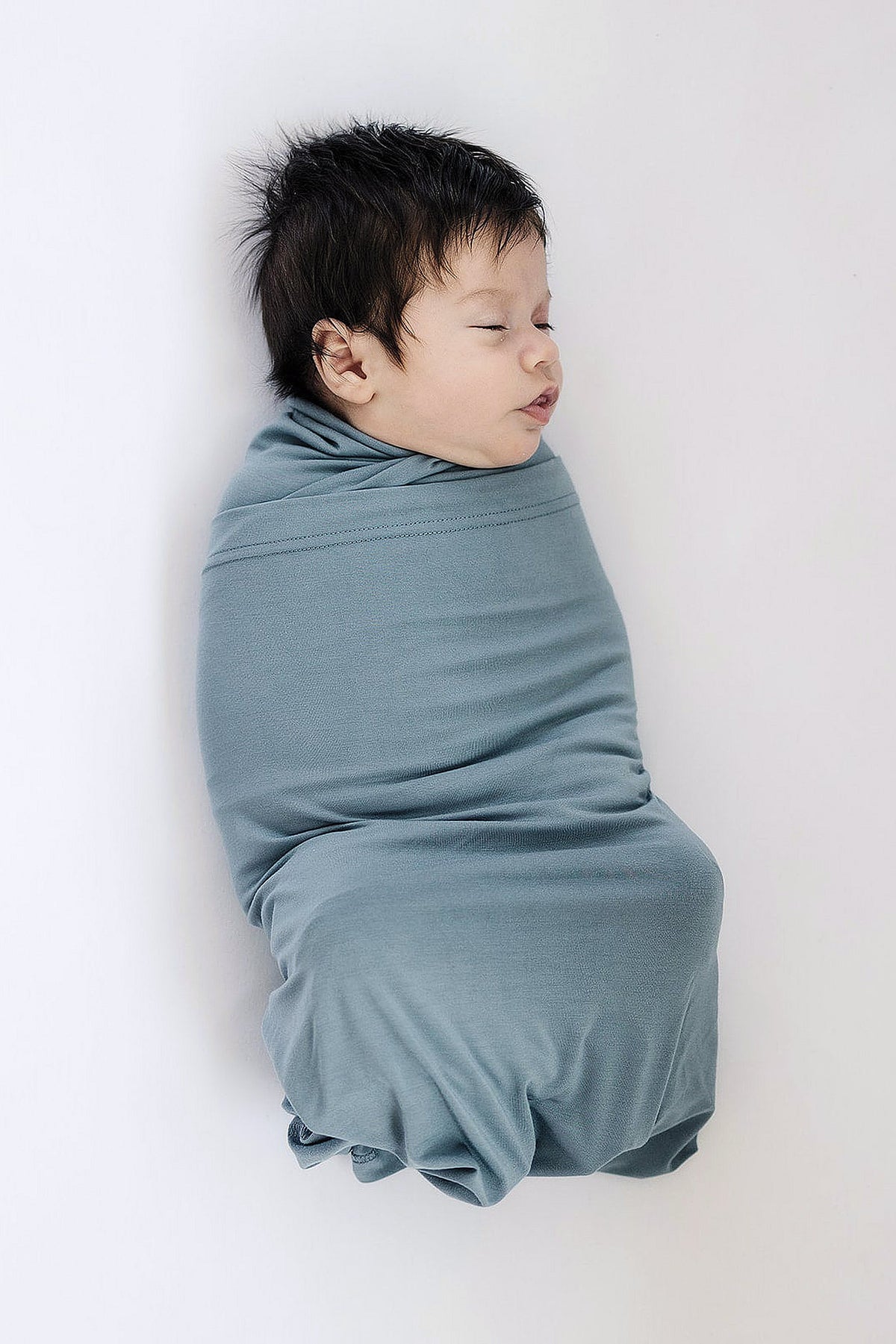 A baby is peacefully swaddled in a dusty blue blanket, showcasing soft, stretchy bamboo fabric.