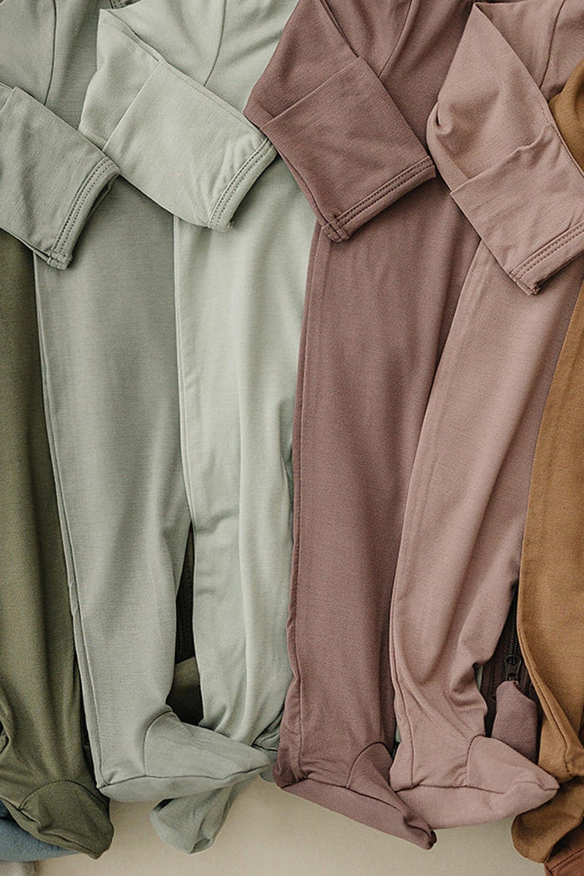 Various shades of bamboo fabric baby footed pajamas are neatly arranged, showcasing their soft texture and muted colors.